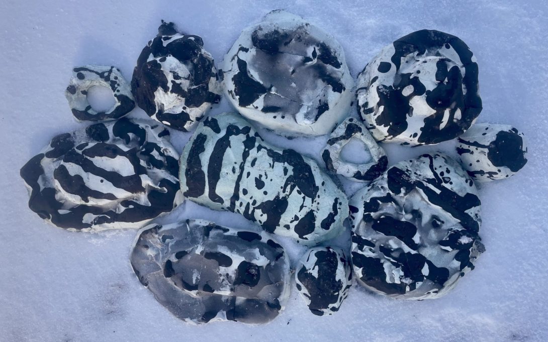 Bird's eye view of light blue and black speckled Bio-Pottery dish set collection puzzle pieced together upside down on snow