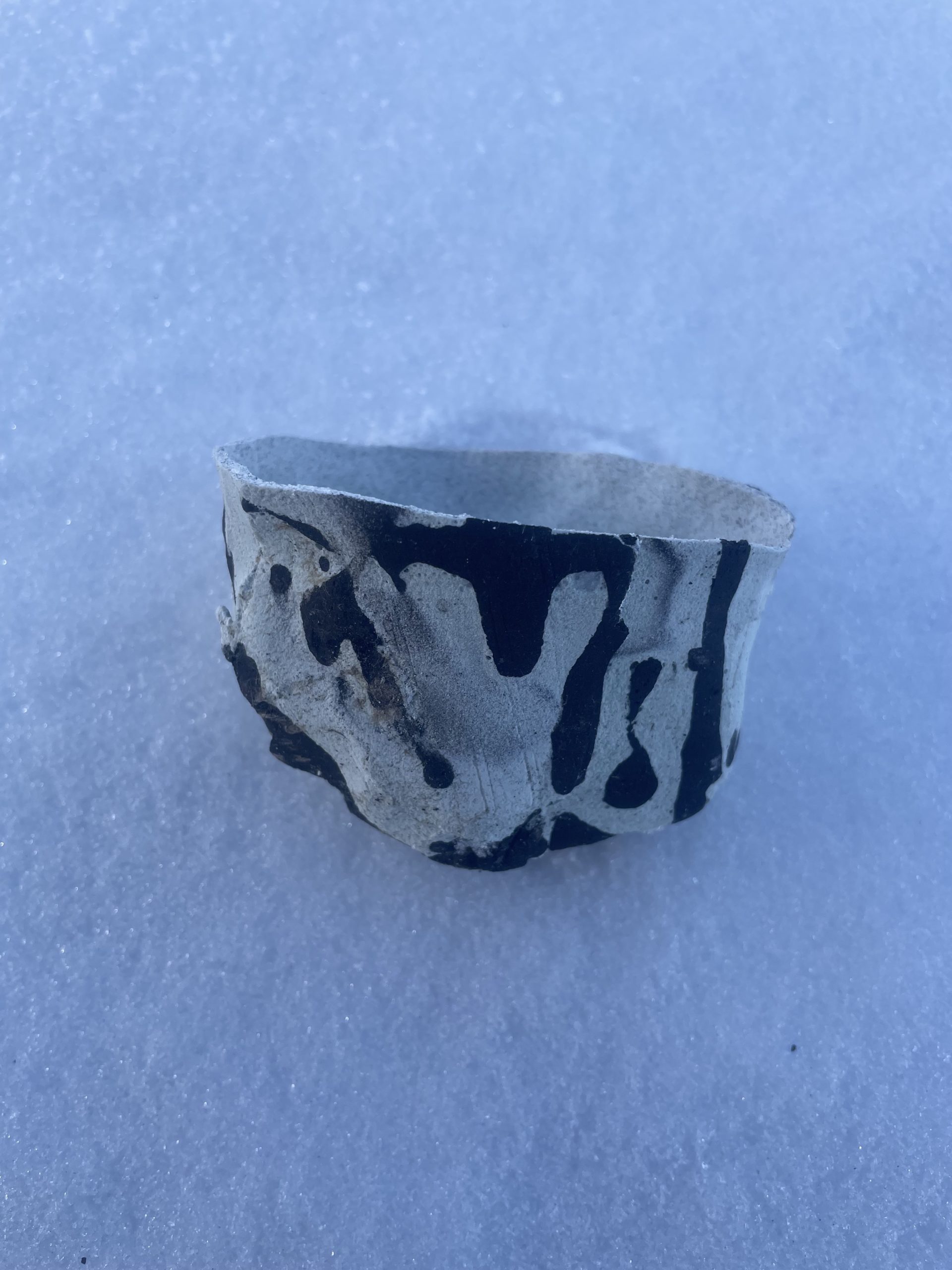 Light blue and black speckled Bio-Pottery cup laying on its side in the snow