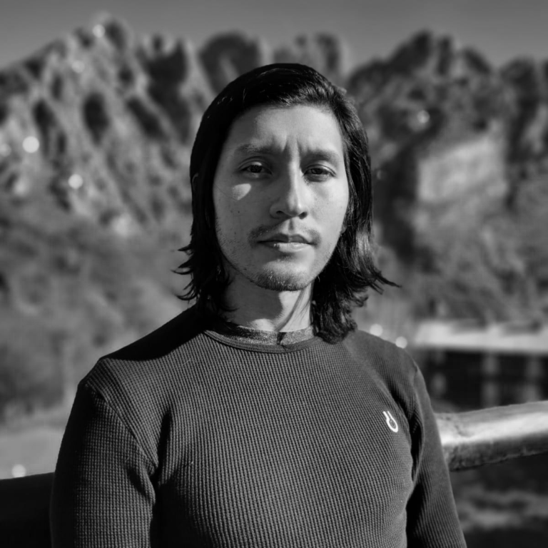 Nico stands in a long-sleeved shirt in front of mountains. Photo in black and white.