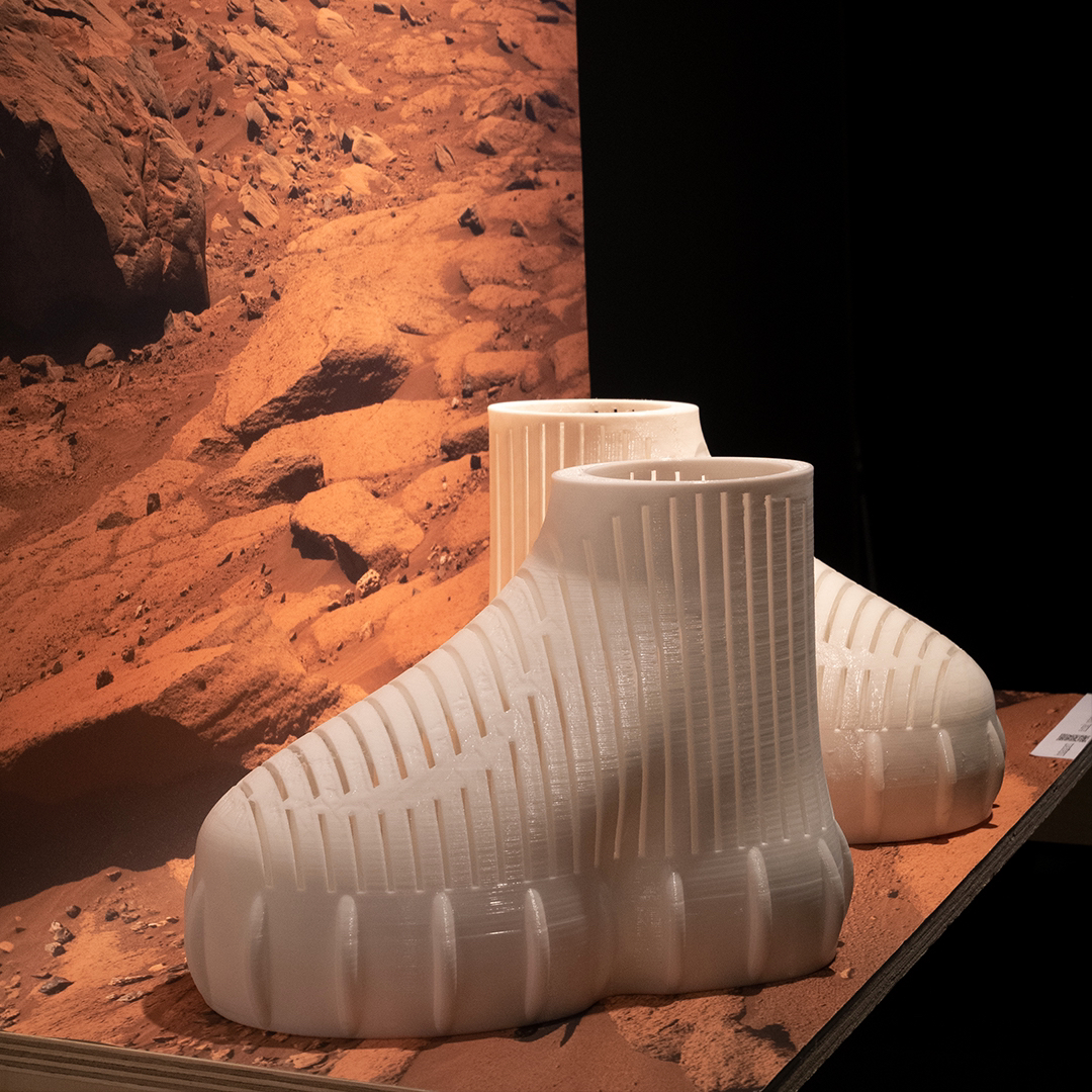 Two white, futuristic running shoes displayed in front of Mars background poster.