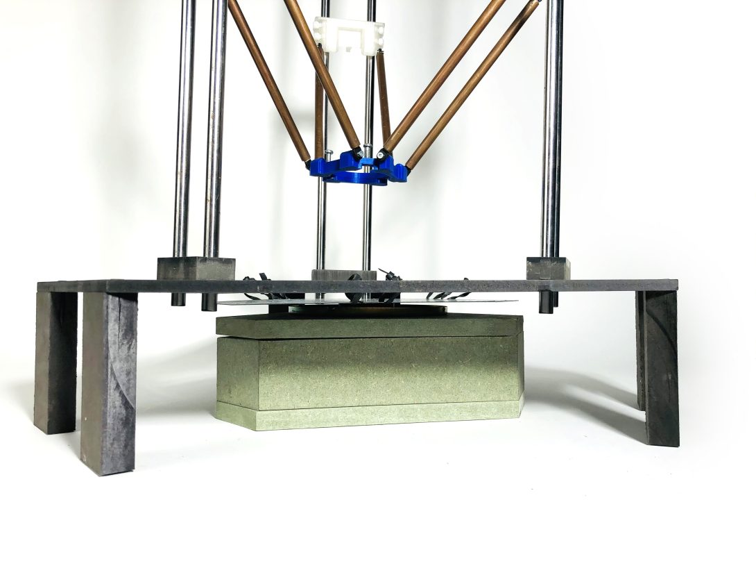 Bottom of the ceramic printer, the plate is made of steel and held using elastic bands, which allows it to move slightly. The printer is triangular in shape. A speaker in a box is placed under the plate.